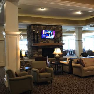 A cozy lobby seating area with sofas, armchairs, a fireplace, and a television.