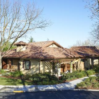 A suburban residential house with a tile roof and surrounding trees on a sunny day.