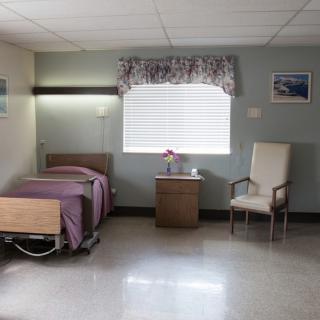 A clean and organized hospital room with a bed, chair, and window.