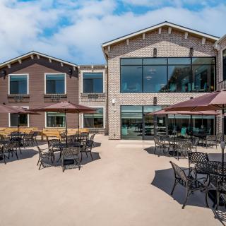 An outdoor patio area with tables and chairs, shaded by umbrellas, outside a modern building.