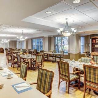 A spacious dining area with neatly arranged tables and chairs, illuminated by chandeliers and natural light from large windows.