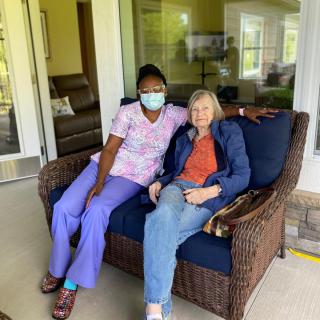A healthcare worker and an elderly person sitting together on an outdoor patio.