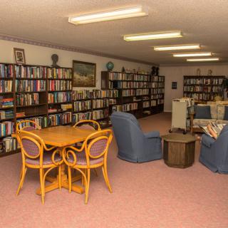 A cozy library with wooden bookshelves, armchairs, and a round table.