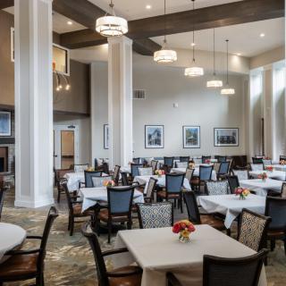 A spacious dining room with neatly arranged tables and chairs, elegantly lit by overhead lights.