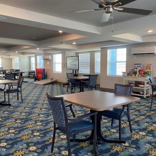 A spacious dining area with several tables and chairs, featuring decorative carpet and ample lighting.
