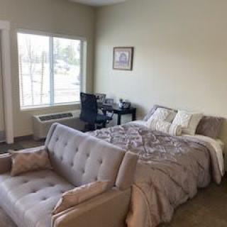 A cozy bedroom with a bed, sofa, and desk by the window.