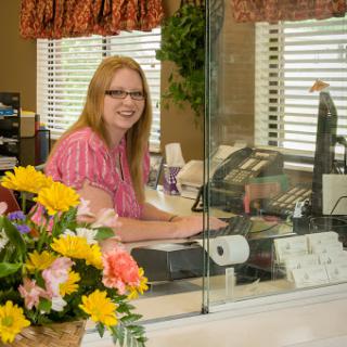 A friendly receptionist at her desk surrounded by vibrant flowers.