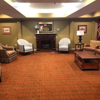 A cozy lounge area featuring comfortable seating, a fireplace, and warm carpeting.