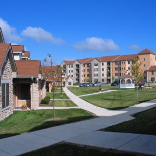 A scenic view of apartment buildings with well-maintained sidewalks and green lawns under a clear blue sky.
