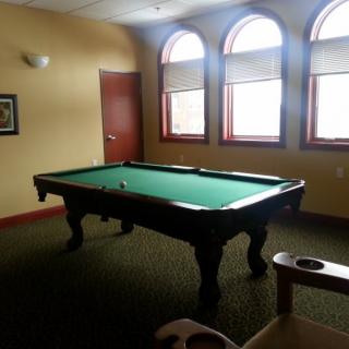 A billiard table in a well-lit game room with arched windows.