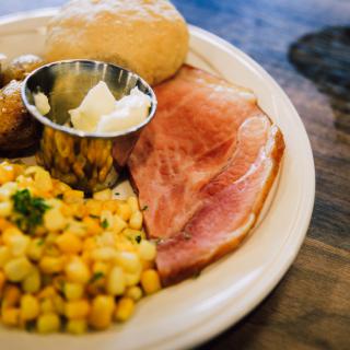 A plate of food featuring ham, corn, bread, and butter.