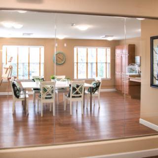 A spacious dining area with a modern kitchen visible in the background, featuring large windows that allow ample natural light.