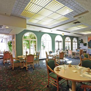 A well-lit dining area with tables and chairs arranged near large windows.