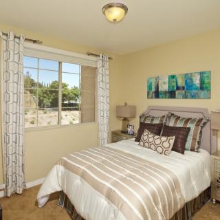 A cozy bedroom with a neatly made bed, decorative pillows, and a window letting in natural light.