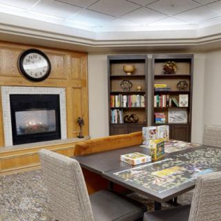 A cozy library room with a fireplace, bookshelves, and a table set up for puzzles.
