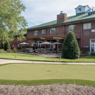 A brick building with a patio and putting green surrounded by trees.