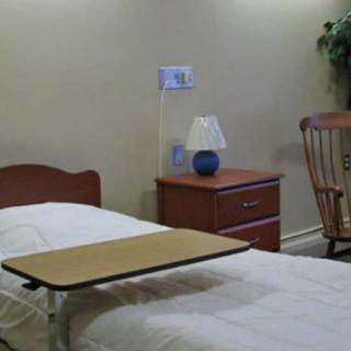 A simple hospital room with a bed, bedside table, lamp, and rocking chair.