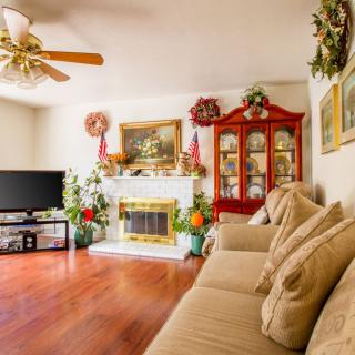 A cozy living room with a sofa, fireplace, and television, featuring warm wooden floors and decorated shelves.