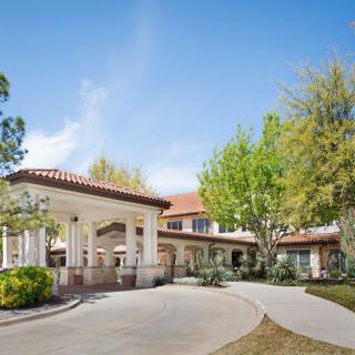 A sunny view of a building entrance with a driveway surrounded by trees.