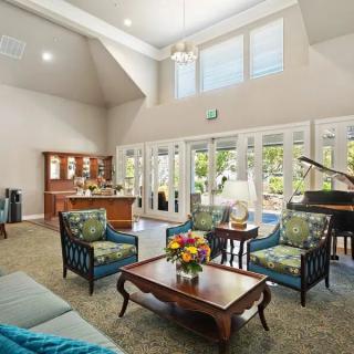 A spacious living room featuring comfortable seating, a piano, and large windows.