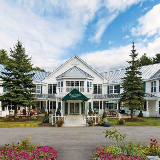 A charming hotel building with a landscaped entrance and vibrant flowers under a cloudy sky.