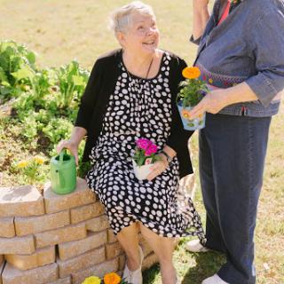 Two women enjoy their time in the garden, surrounded by colorful flowers and greenery.