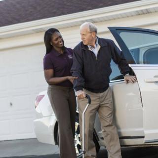 A caregiver assists an elderly man as he exits a car.