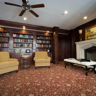 A cozy library room with bookshelves, armchairs, and a fireplace.