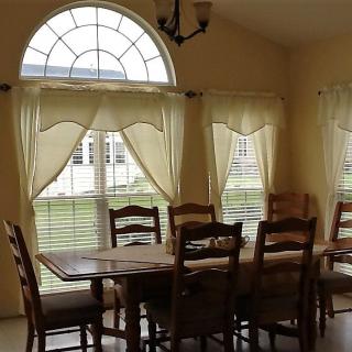 A cozy dining room with a wooden table and chairs, featuring large windows with curtains.