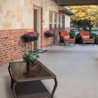 A cozy patio with seating and plants against a brick wall.