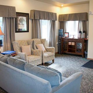A cozy living room with comfortable seating, a cabinet, and large windows with curtains.
