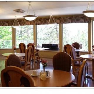 A well-lit dining room with round tables and cushioned chairs, featuring large windows that allow natural light to fill the space.