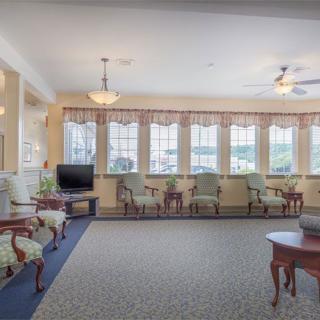 A spacious living room with traditional decor, featuring a seating area, large windows, and a television.