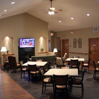 A cozy dining area with tables, chairs, and a large TV screen on the wall.
