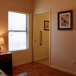 A cozy bedroom with wooden flooring, a window allowing natural light, and decorative frames on the wall.