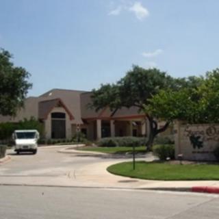 A building with a driveway and van parked in front, surrounded by trees and landscaping on a sunny day.