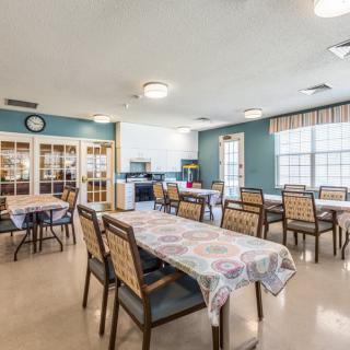 A well-lit dining room with multiple tables and chairs, featuring large windows.