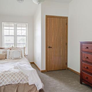 A cozy bedroom with a bed near a window, a wooden dresser, and a closed door.
