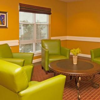 A cozy seating area with bright green chairs and a round table, set against vibrant orange walls.