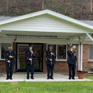Members of the honor guard perform a salute in front of a building.