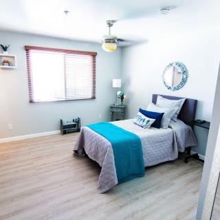 A modern minimalist bedroom featuring a single bed with blue and gray bedding, wooden flooring, and simple decor.