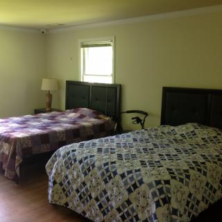 A cozy bedroom with two beds adorned with patterned quilts, a small window, and a lamp.