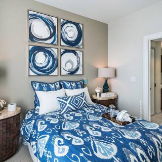 A modern bedroom featuring blue-toned bedding and abstract artwork on the wall.