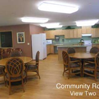 A community room featuring a kitchen area with tables and chairs.