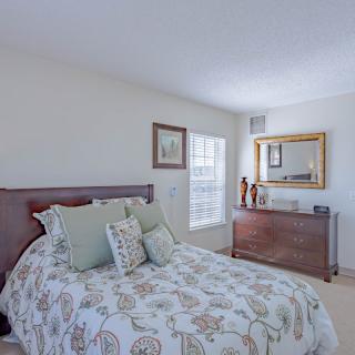 A cozy bedroom with a neatly made bed, a dresser with a mirror above it, and soft natural light from the window.