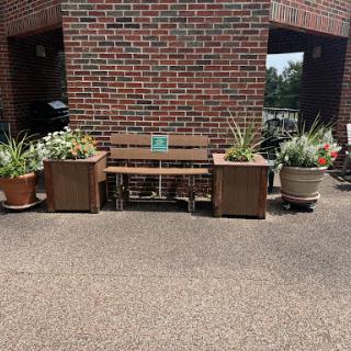 A cozy outdoor seating area featuring a wooden bench surrounded by lush planters against a brick wall.