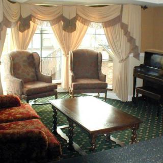 A cozy living room featuring two armchairs, a coffee table, and a piano, with elegant curtains framing the windows.
