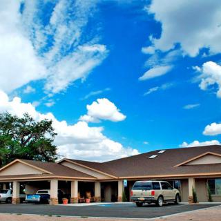 A view of a motel with a parking lot and cars under a partly cloudy sky.