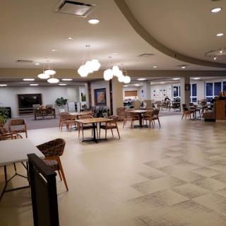 A spacious and modern lounge area with tables and chairs, featuring warm lighting.