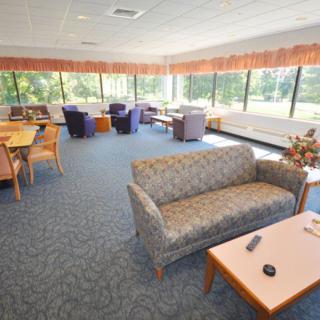 A spacious lounge with sofas, tables, and chairs, featuring large windows.